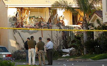 LAPD investigators look at the back of the Sylmar house Tuesday morning where a gunman suspected of critically wounding a Los Angeles police officer was found dead Monday night. The man had been holed up for nearly a day in the house as authorities fired tear gas and finally used a hydraulic forklift to rip open the home's walls. (Al Seib / Los Angeles Times / April 5, 2011)