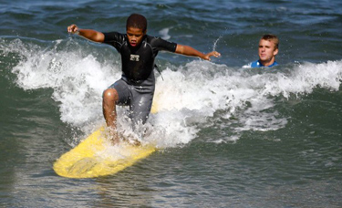 Donovan West, 12, catches a wave with the help of professional surfer Matt Pagan, 23, at Torrance Beach. (Luis Sinco, Los Angeles Times / August 2, 2011)