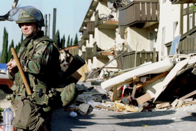 A National Guardsman stands outside the ruins of the Northridge Meadows Apartments where 16 people died on Jan. 17, 1994.Credit AFP / Getty context