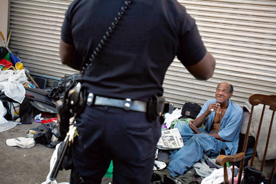 A Los Angeles police officer speaks to a man on skid row sitting among the kind of items that the city's Safer City Initiative had largely cleared from the sidewalks. (Barbara Davidson / Los Angeles Times)